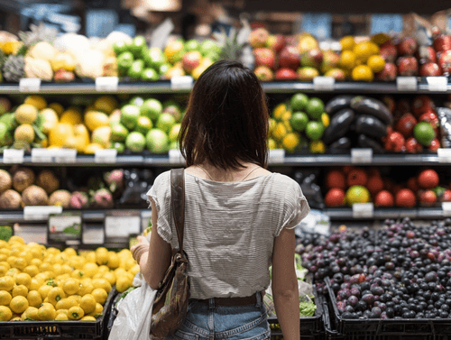 A woman in front of fruits and vegetables tring to decice which one to buy